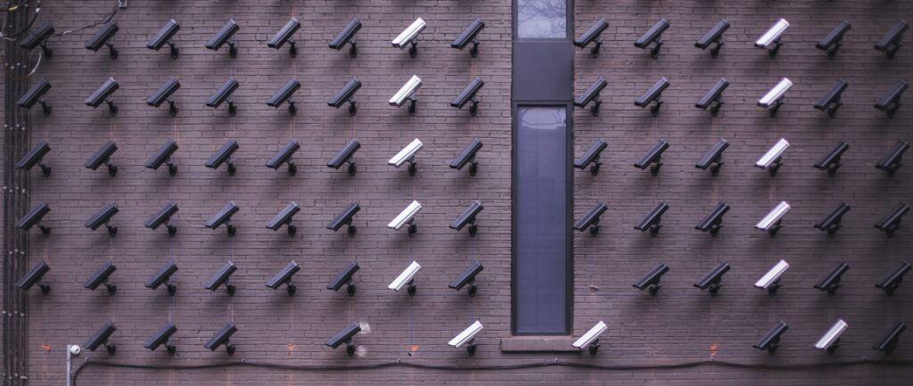 A vast array of surveillance cameras look down on two women who are looking up at them.